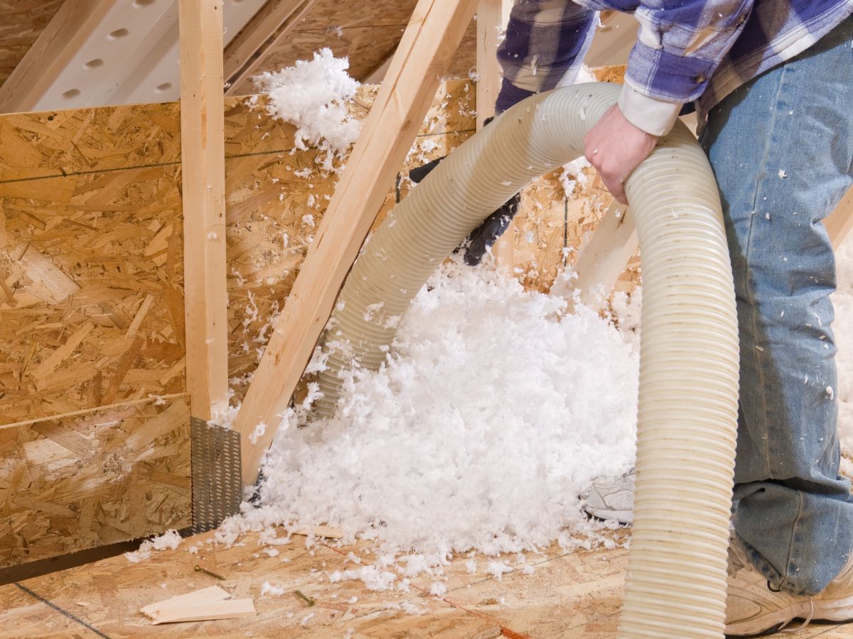 A man operates a vacuum cleaner to remove insulation from a floor, focusing on cleaning the area thoroughly.