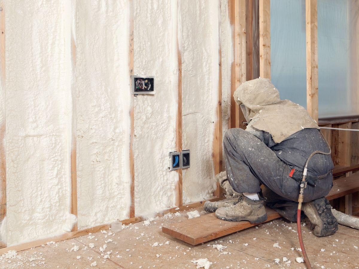 A man installs insulation on a wall, using tools and materials to enhance energy efficiency in a construction project.