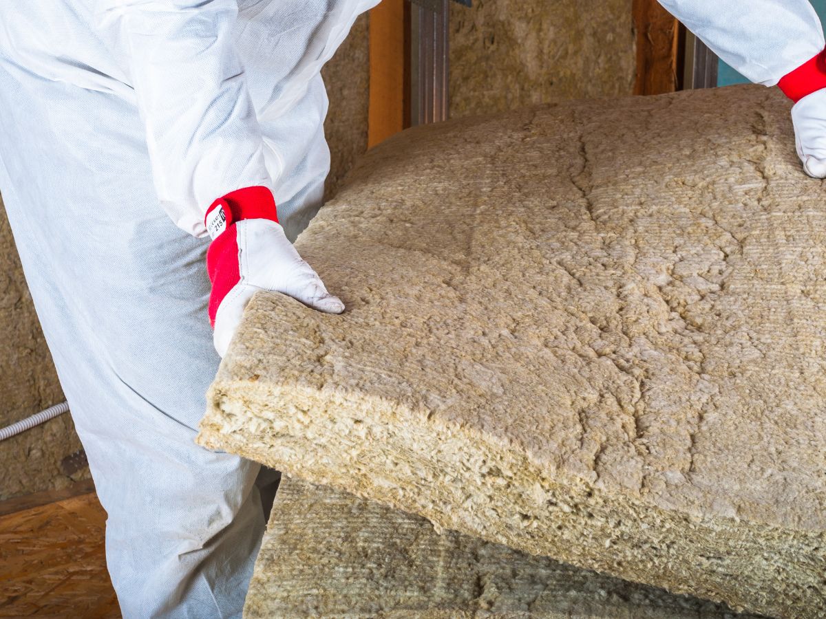 A man in a white suit and red gloves holds a large piece of insulation, standing against a neutral background.