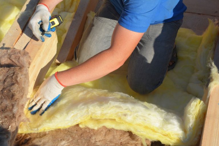 A man installs insulation on a wooden floor as part of an insulation service project.