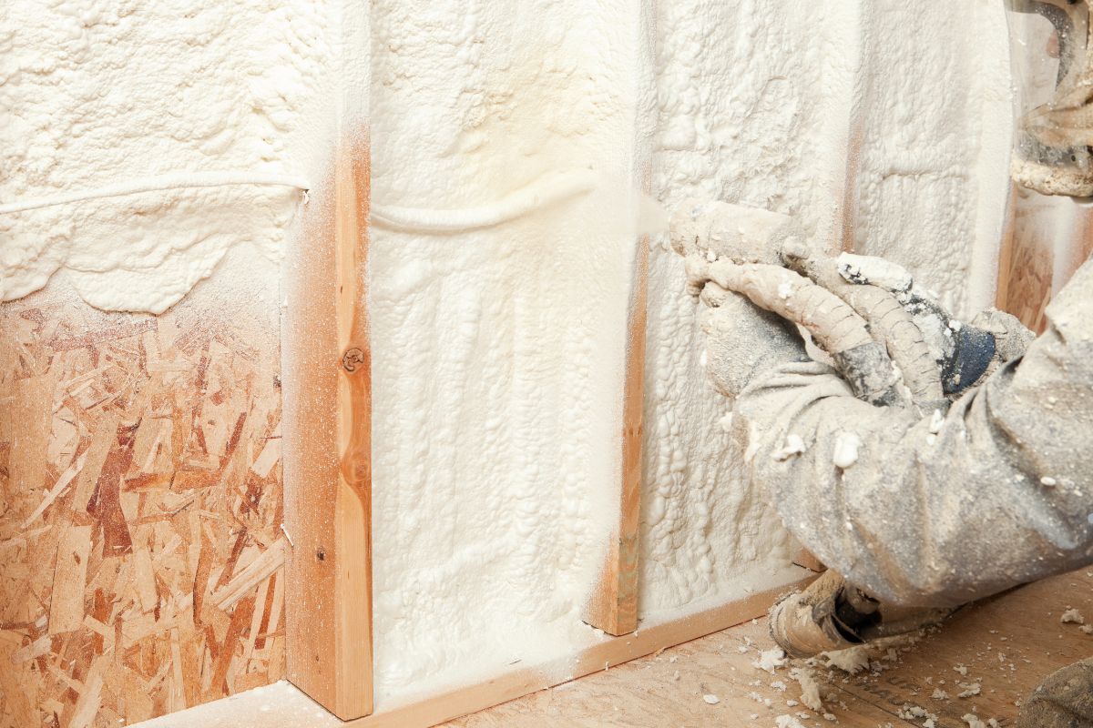 A man applies insulation using a spray gun, demonstrating an insulation service in action.